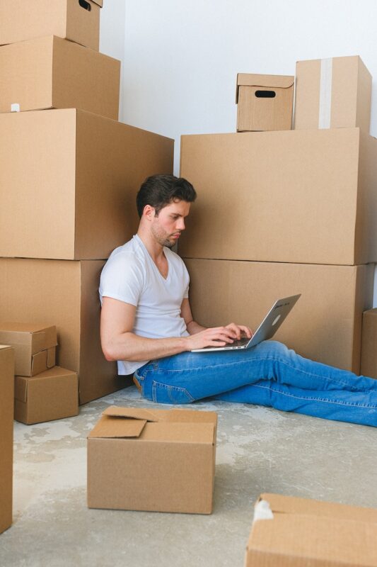 Focused guy working distantly on netbook sitting on floor near carton boxes